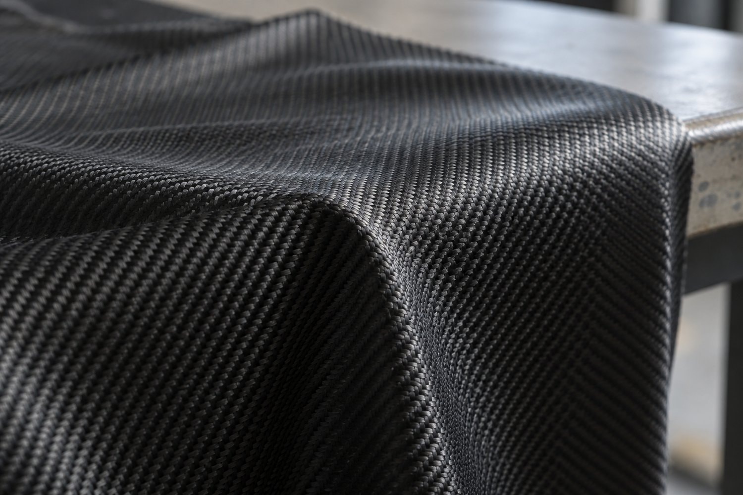Dark twill-weave carbon fabric draped across the edge of a workbench.
